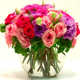 Round glass vase of pink roses, purple lisianthus, and pink carnations in a compact arrangement