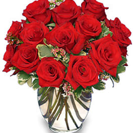Dozen red roses with small pink filler flowers arranged in a clear glass vase
