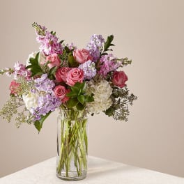 Tall bouquet of pink roses, lavender stock, and white hydrangeas in a clear glass vase