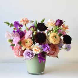 Mixed bouquet of pink, purple, peach, and white flowers in a pale green vase