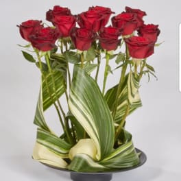 Red roses arranged with striped leaves in a low black container