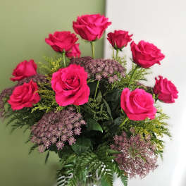 Pink roses arranged in a clear glass vase with purple filler flowers