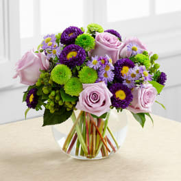 Pink roses and purple-green mixed flowers in a clear glass vase