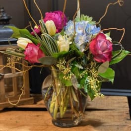 Mixed bouquet of pink, white, and blue flowers in a glass vase