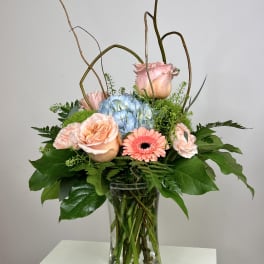 Pink roses and a blue hydrangea in a clear glass vase