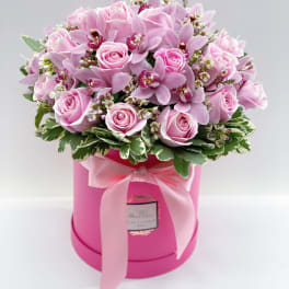 Pink roses and orchids arranged in a round pink box with a ribbon