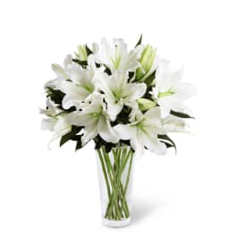 Tall clear vase of white lilies with green buds and stems