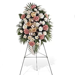 Tall standing spray of white daisies, peach roses, and pink carnations on a metal easel