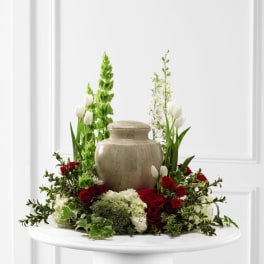 Cremation urn encircled by red roses, white tulips, and white hydrangeas with tall green floral spikes.