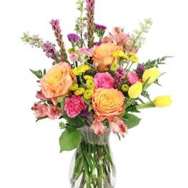 Mixed bouquet of peach roses, pink flowers, and yellow tulips in a glass vase