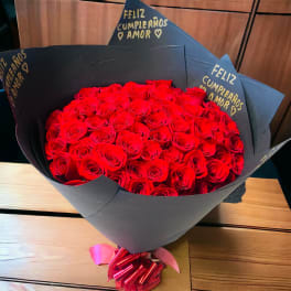 Large bouquet of red roses wrapped in black paper with a pink ribbon