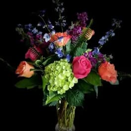 Mixed bouquet of roses, hydrangea, and blue flowers in a glass vase