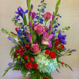 Tall mixed bouquet in a clear glass vase with pink roses and blue flowers