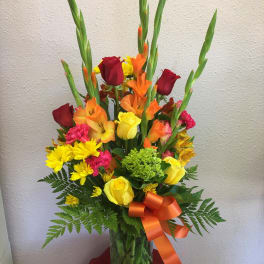Tall mixed bouquet of roses, gladiolus, and daisies in a glass vase