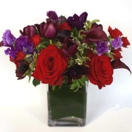 Red roses and purple flowers in a square glass vase