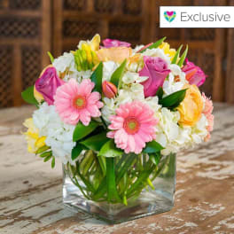 Mixed pink, white, and yellow flowers in a clear square vase
