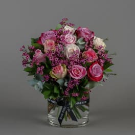 Pink and white roses in a clear glass vase with a ribbon