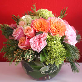 Low arrangement of pink and orange roses with green hydrangea in a round glass vase