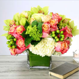 Compact mix of pink and peach roses, green orchids, and white hydrangeas in a square glass vase