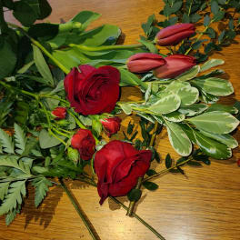 Red roses and pink tulips with assorted greenery on a wooden surface