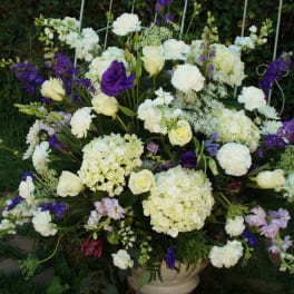 Large white and purple floral arrangement in a cream vase