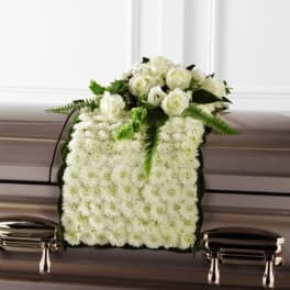White rose and chrysanthemum casket spray draped over a bronze casket