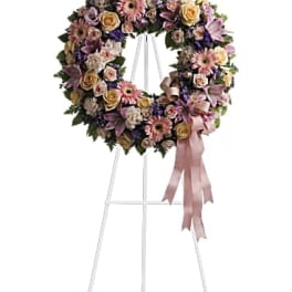 Pastel floral wreath with roses, gerberas, and lilies on a white easel with pink ribbon