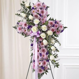 Standing cross-shaped spray with pink and purple mums and white roses on an easel.