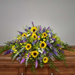 Bright casket spray of yellow sunflowers and mixed purple and white flowers on a wooden casket