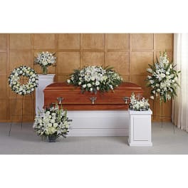 Set of white floral funeral arrangements around a wooden casket in a chapel.
