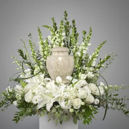 White lilies and roses arranged around a stone urn with tall white snapdragons behind.