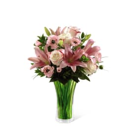 Pink lilies and roses arranged in a tall green glass vase
