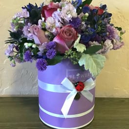 Pink and purple flower arrangement in a lavender hat box with a white ribbon