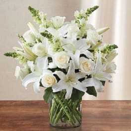 Arrangement of white lilies, roses, and snapdragons in a clear glass cylinder vase