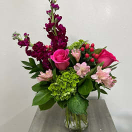 Bouquet of pink roses, green hydrangea, and purple blooms in a glass vase