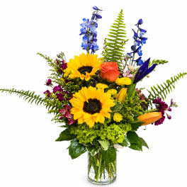 Bright mixed bouquet with sunflowers, roses, and blue flowers in a glass vase