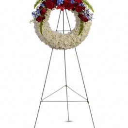 Standing funeral wreath with red roses, white flowers, and blue accents on an easel