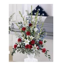 Standing floral spray with red, white, and blue flowers in a white urn