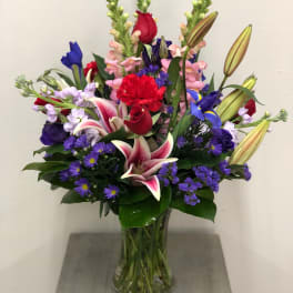Mixed bouquet of lilies, roses, and purple filler flowers in a glass vase