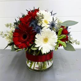 Red and white gerbera daisies in a glass vase with a red ribbon
