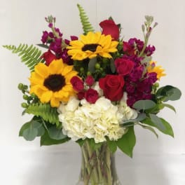 Bouquet of sunflowers, red roses, and white hydrangeas in a glass vase