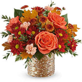 Autumn bouquet of orange roses and red daisies in a woven basket