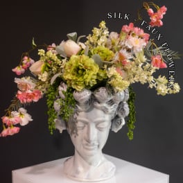 Silk floral arrangement in a white bust vase with pink and green blooms
