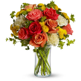 Bouquet of orange and coral roses with yellow mums and white carnations in a clear glass vase