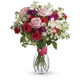 Pink and white bouquet with roses and lilies in a clear vase with a pink butterfly accent