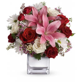 Mixed arrangement of pink lilies, red and white roses, and white daisies in a clear glass cube vase