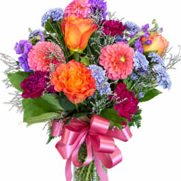 Colorful bouquet of roses, dahlias, and purple flowers in a glass vase with a pink ribbon