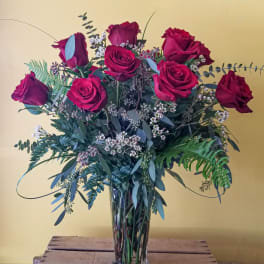 Red roses arranged in a clear glass vase with mixed greenery