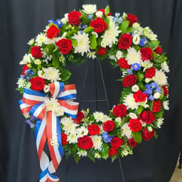 Circular wreath of red, white, and blue flowers with a ribbon bow