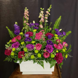 Pink and purple floral arrangement in a white rectangular planter